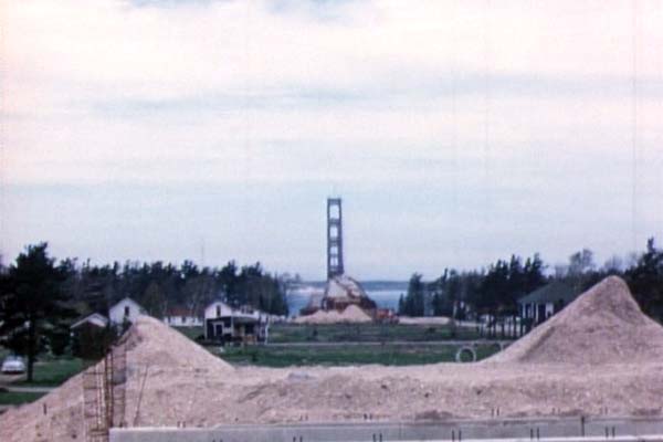 A shot from the partially-complete Central Avenue overpass in Mackinaw City looking north. The Mackinac Bridge is within 18 months of being complete, yet the southern approach is just underway. Trees and structures have been cleared, but additional fill is needed. (Spring 1956)