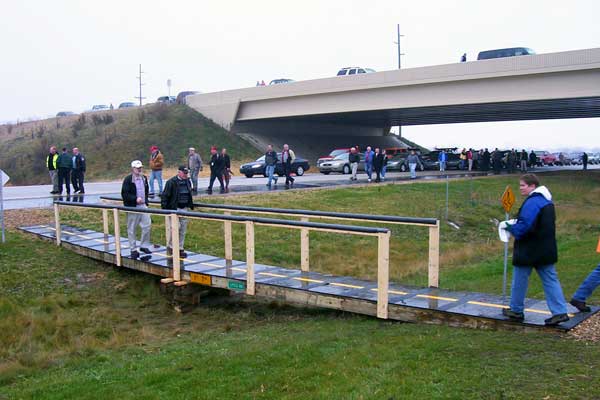 Another view of the pedestsrian bridge spanning the median, this time from the westbound lanes. Event attendees are arriving en masse now and other spectators and local citizens are beginning to gather on the Byron Center Ave overpass above.